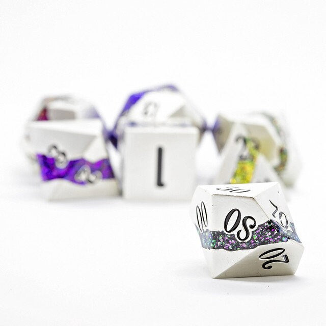 Closeup of a d00 metal polyhedral dnd dice in silver metal with a beautiful stripe of glittery purple and green resin with other rainbow striped dice in the background.