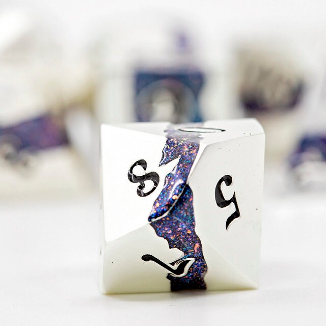 Closeup of a d10 with other metal polyhedral dnd dice in pearl silver metal with beautiful stripes of glittery blue and pink resin in the background.